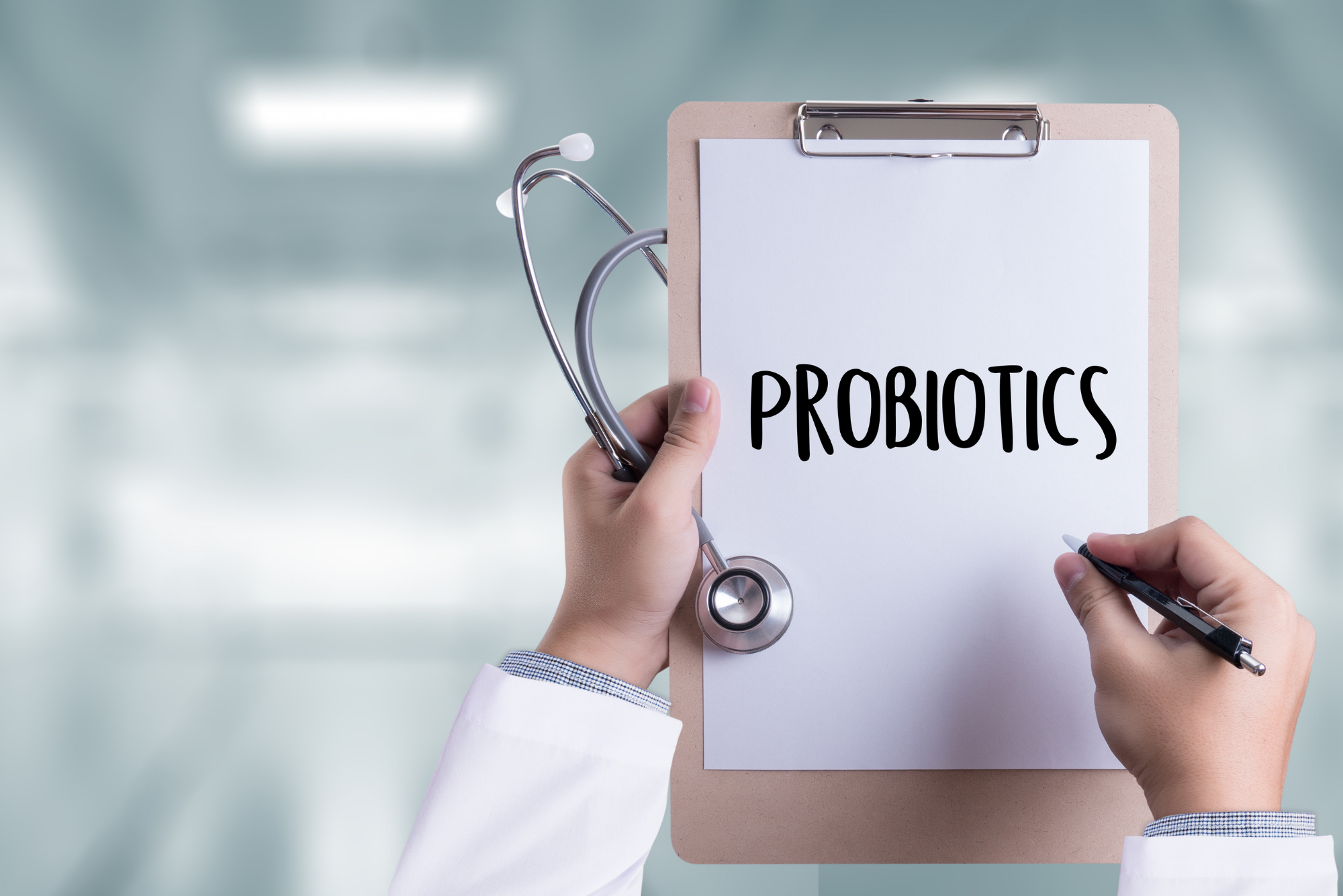 A physician holding a clipboard writes on a piece of paper to tell a patient that they can take probiotics with antibiotics.