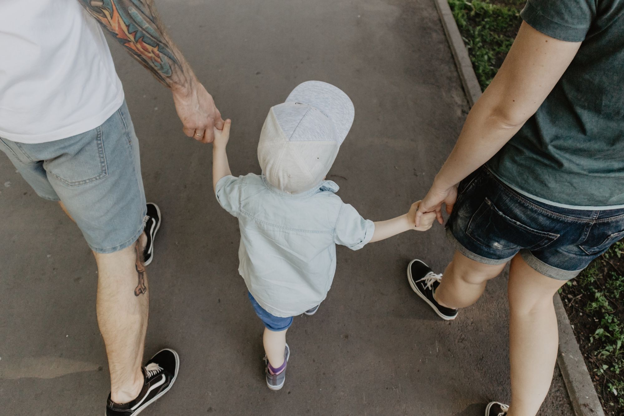 Two parents walk with their toddler in a white hat, telling him health lessons for kids.