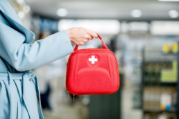 A person in a blue coat holds a red first aid kit containing 20 items.
