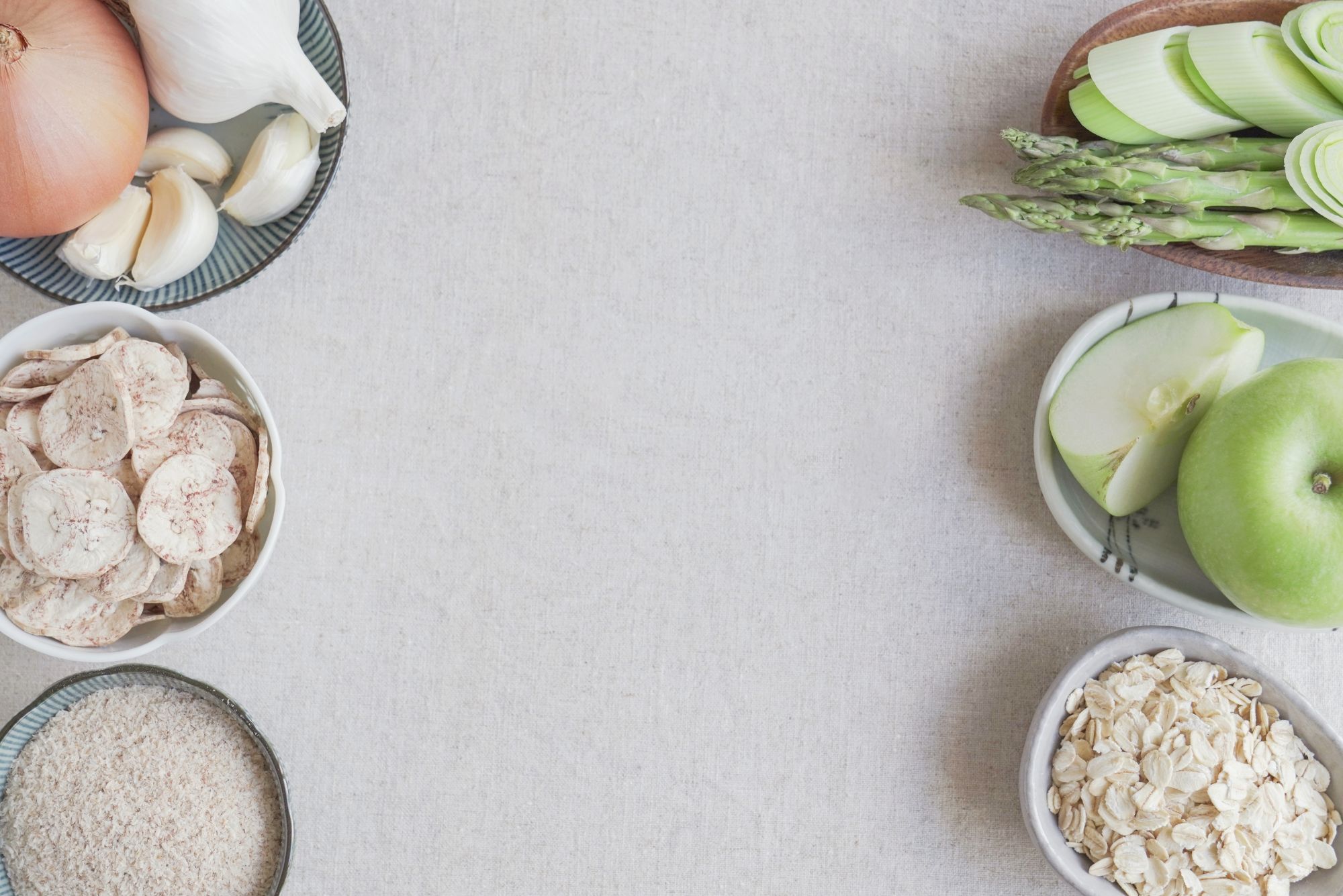 Food helpful for your human microbiome is spread out on a white table in various bowls.