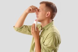 A man in a green shirt pinches his nose after learning how to stop a nosebleed.