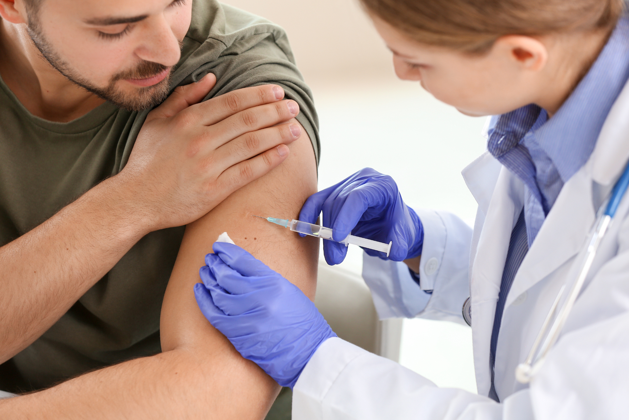 After learning the difference between bacterial vaccines vs. viral vaccines, a man in a green shirt receives a vaccine from his doctor.