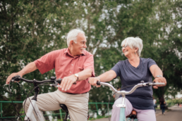 An older couple rides bikes together on a sunny afternoon to maintain their health and lower their metabolic age.