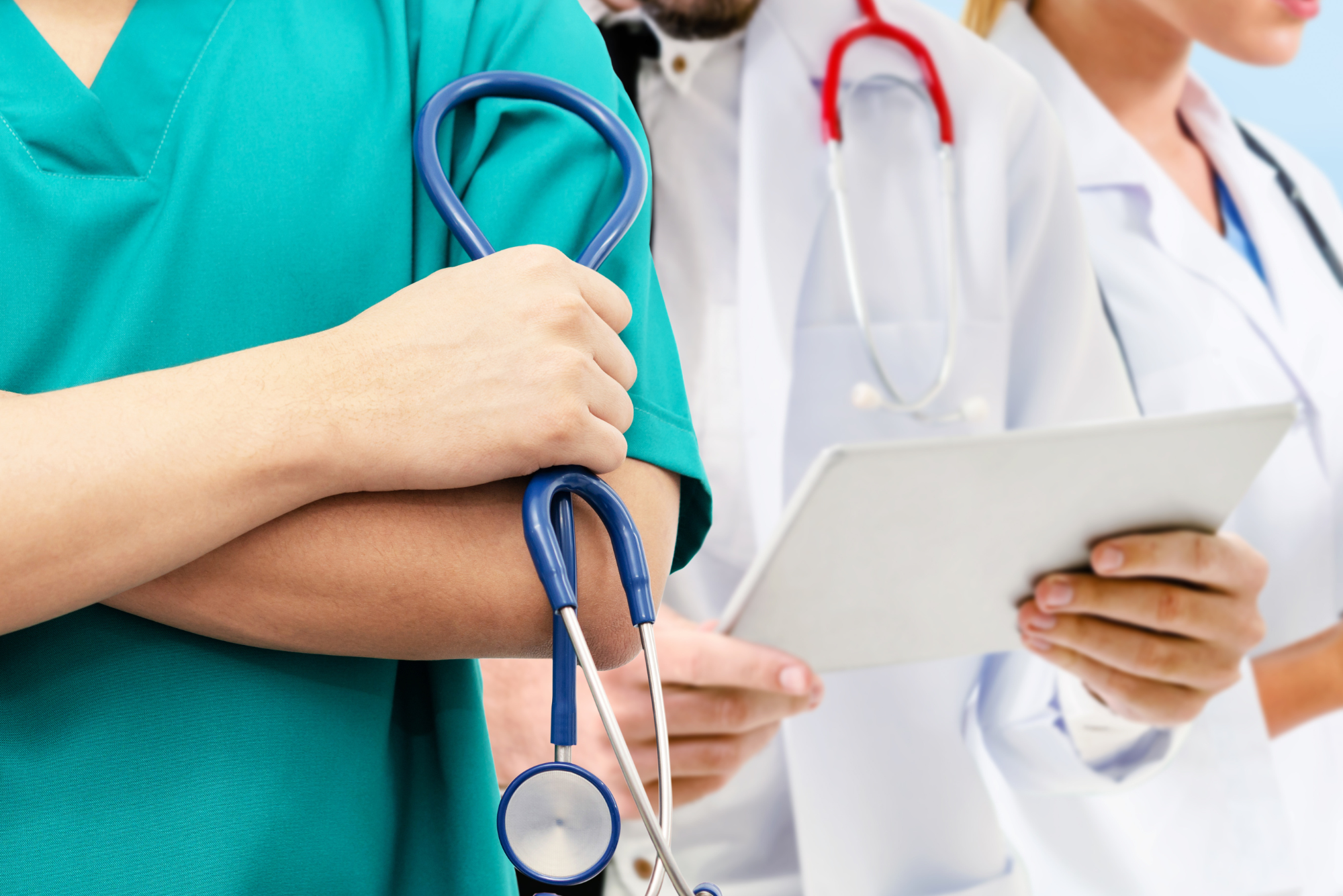 A doctor in green scrubs stands holding a stethoscope with two other doctors, discussing outdated medical practices.