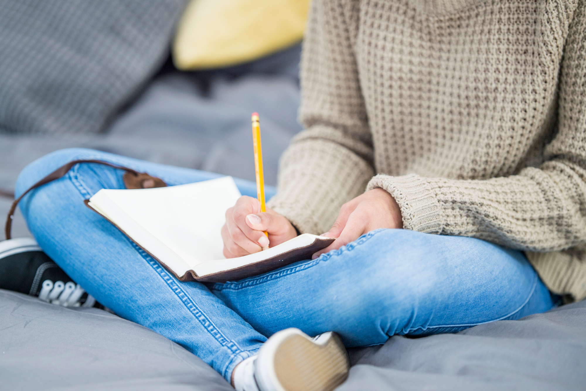 A woman sits indian style, with her journal in her lap, writing in it, after learning how journaling can help mental health.