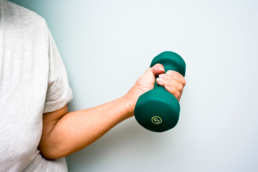 A person lifts a green five pound dumbell, showing what happens when you exercise.