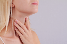 A blond woman holds her throat where her thyroid is before going to the doctor to learn how to balance thyroid hormones.