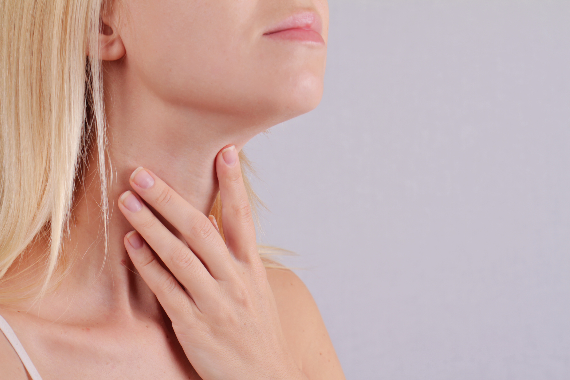 A blond woman holds her throat where her thyroid is before going to the doctor to learn how to balance thyroid hormones.
