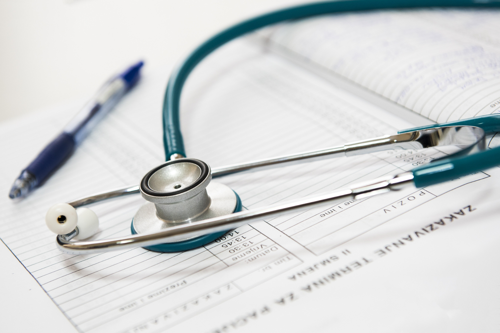 A green stethoscope lies curled on a blank medical chart next to a pen.