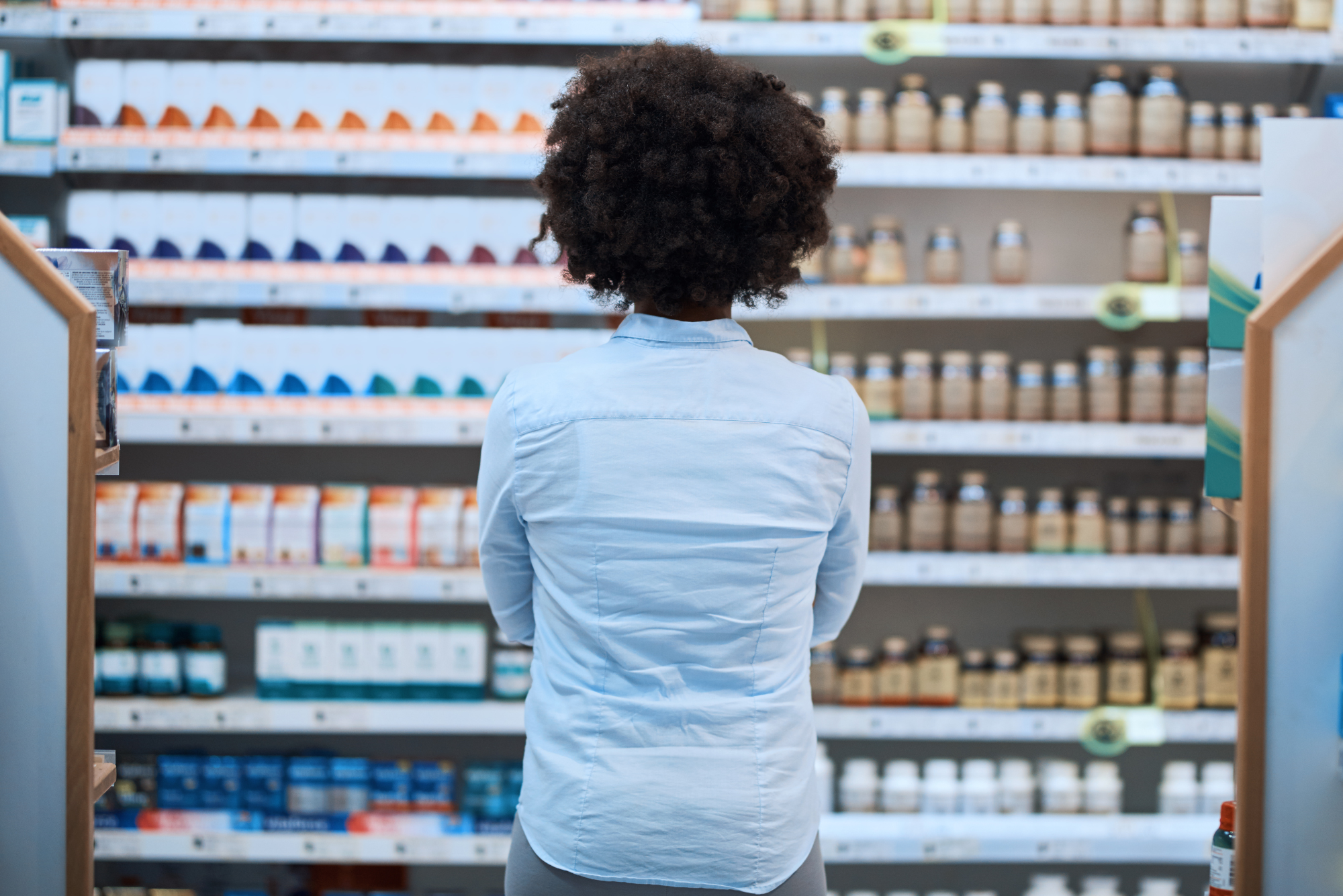 A woman stands in front of a wall of pills thinking about the pros and cons of Metformin.