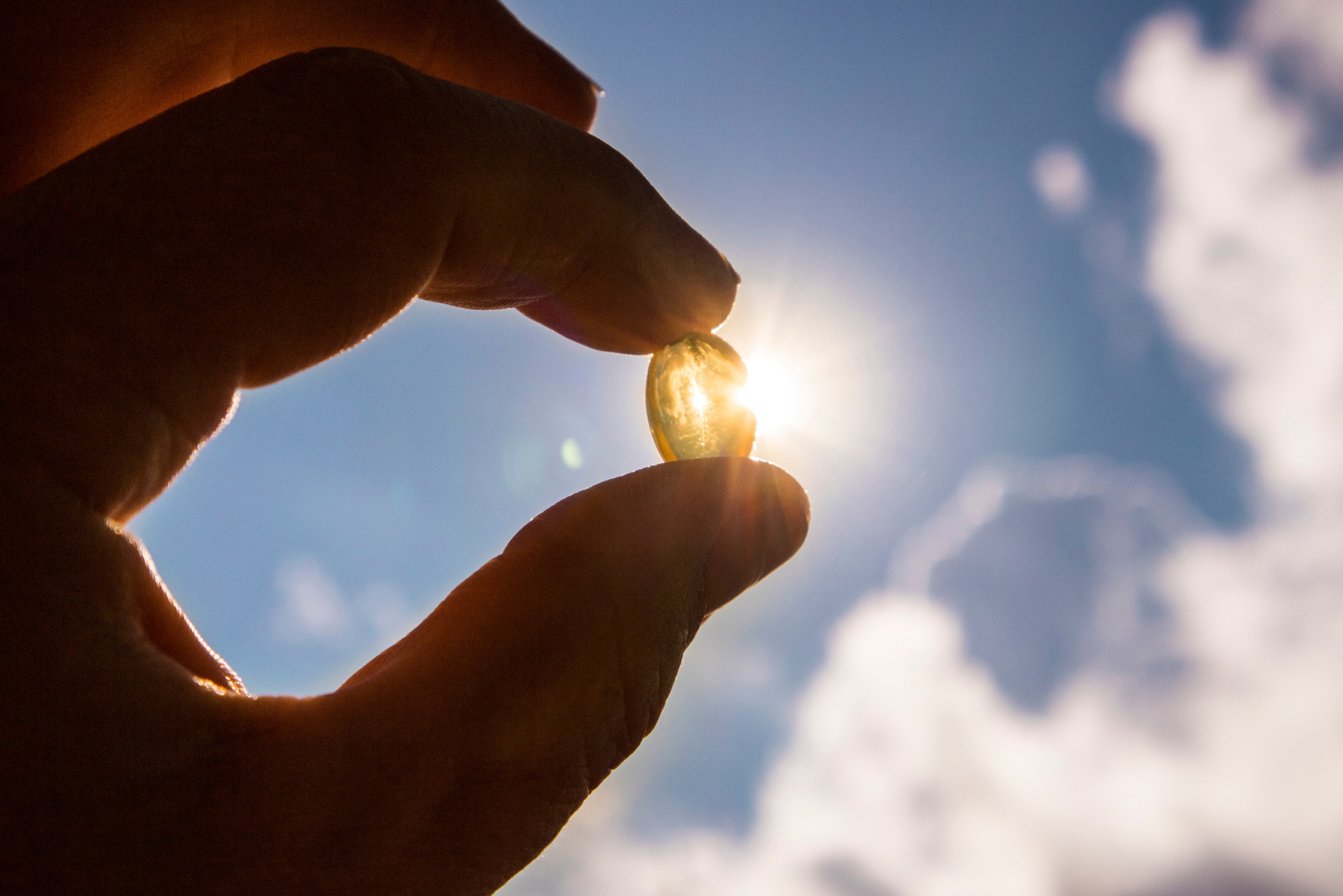 A person holds their hand in front of a sunny sky while holding vitamin D supplements.