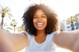 A woman smiles widely at the camera while taking a selfie.