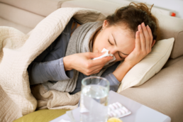 A woman lays on her couch with a high fever, blowing her nose, trying to identify her red flag symptoms.