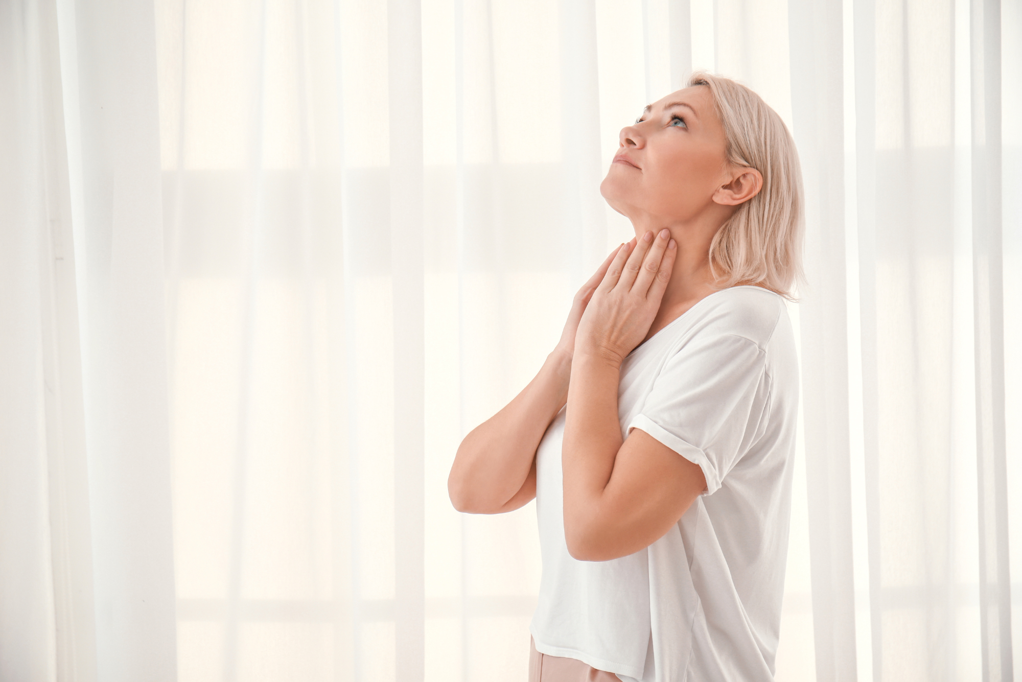 A woman holds her neck where her thyroid is because she has had thyroid problems due to emotional trauma.