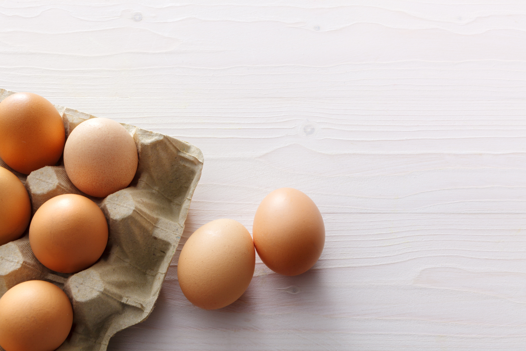 A carton of fresh brown eggs sits on a wooden table top, representing the nutritional value of eggs.