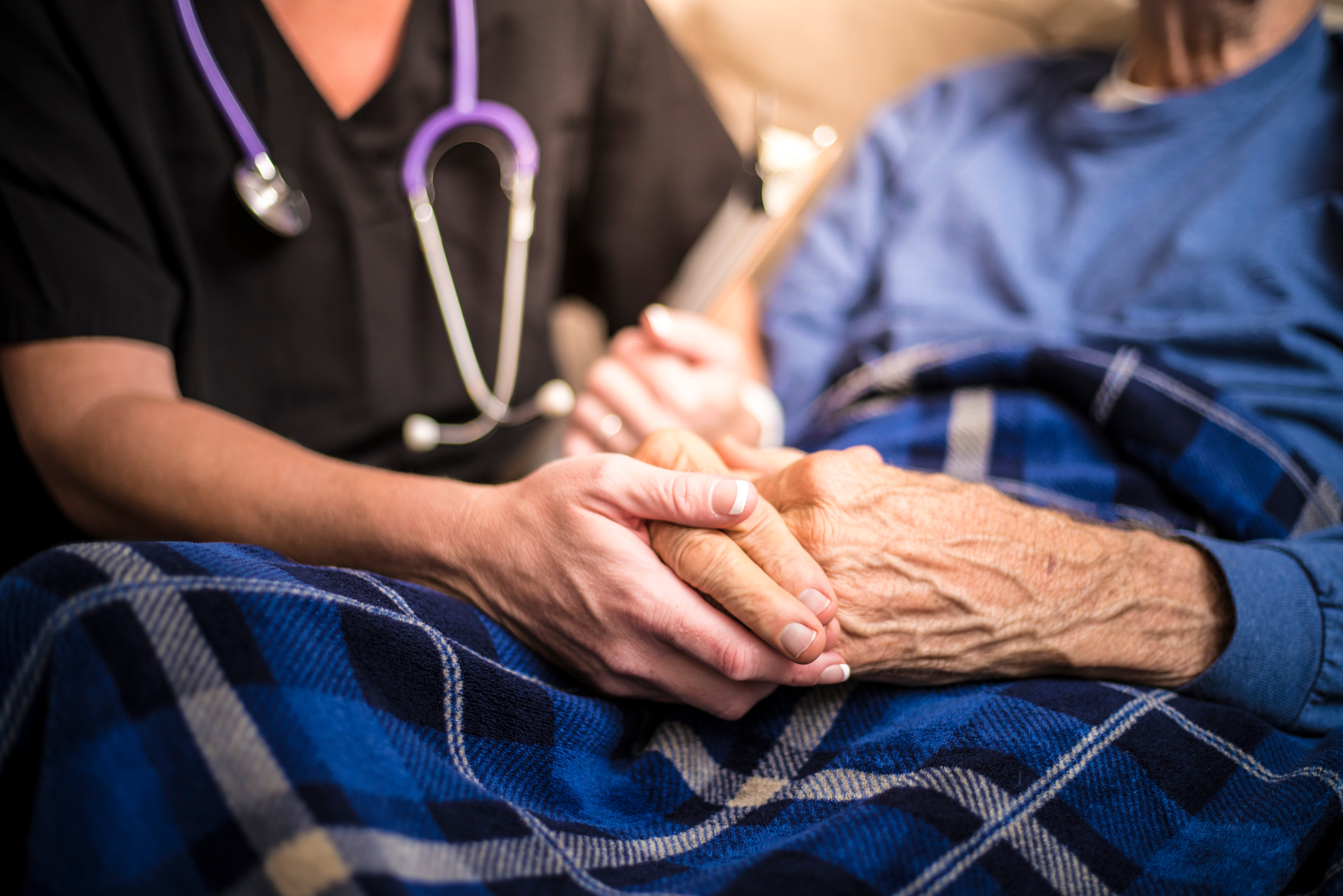 A palliative care nurse holds the hands of one of her elderly patients.