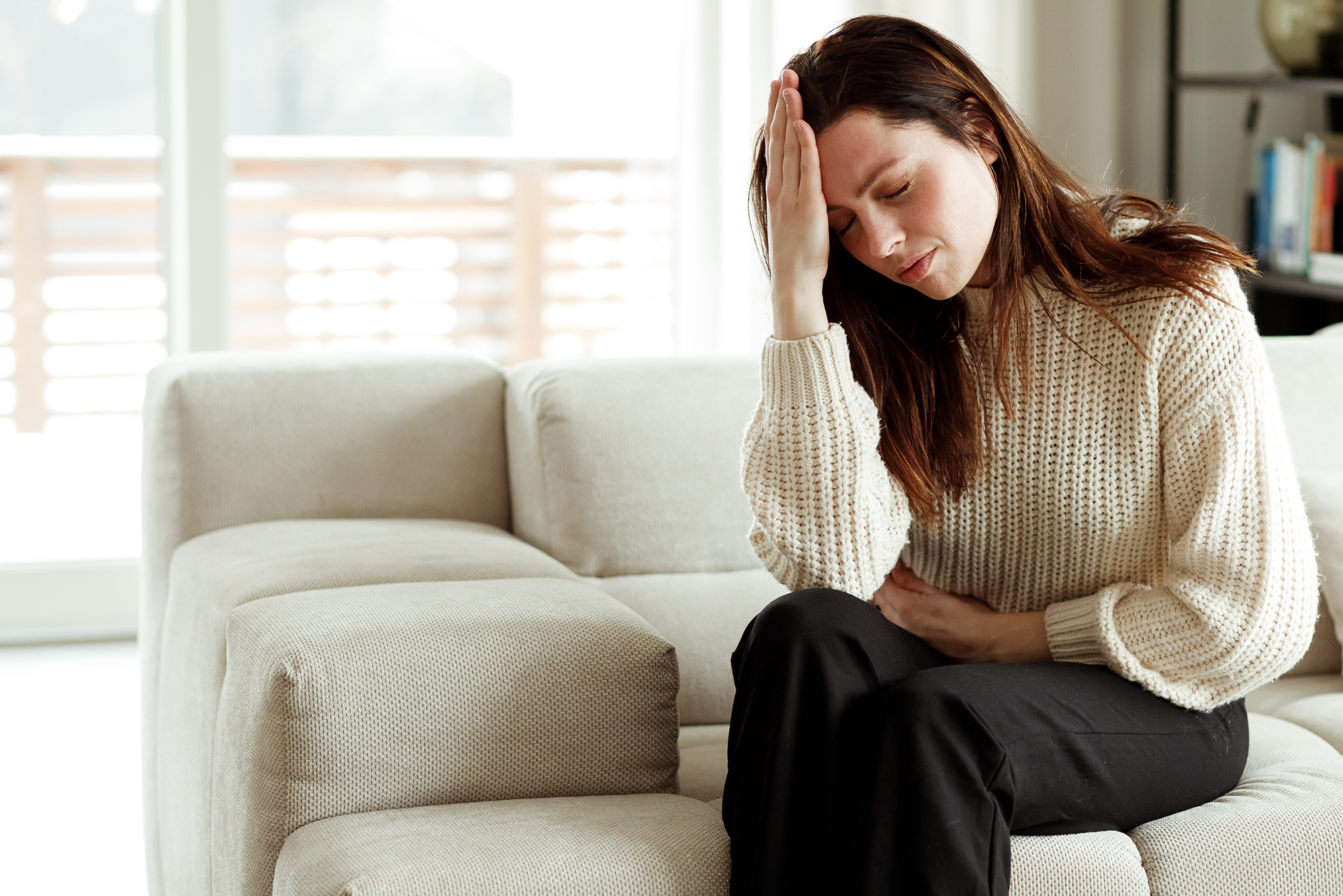 A woman sits on her couch, holding her head in her hands because she has a migraine.