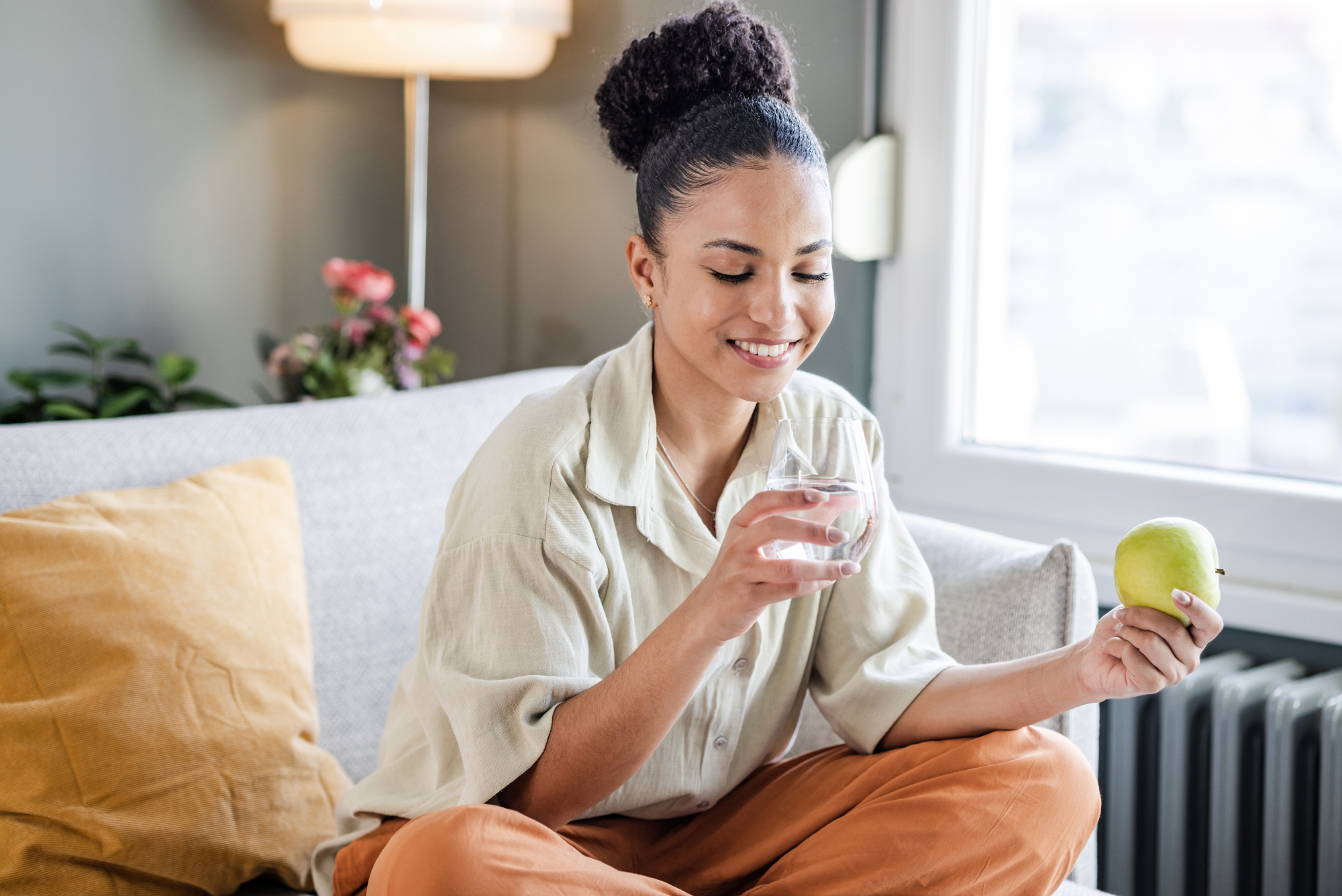 For an afternoon snack, a woman chooses an apple and a large glass of water because she wants to develop healthy habits.