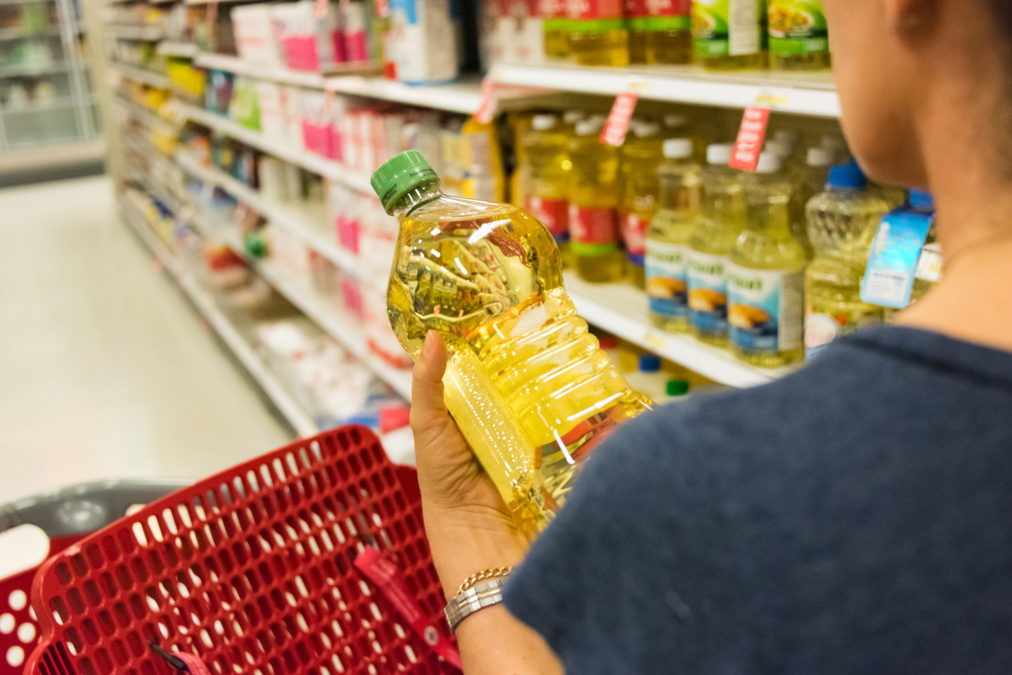 Person holding a bottle of vegetable oil while shopping in a grocery store aisle.