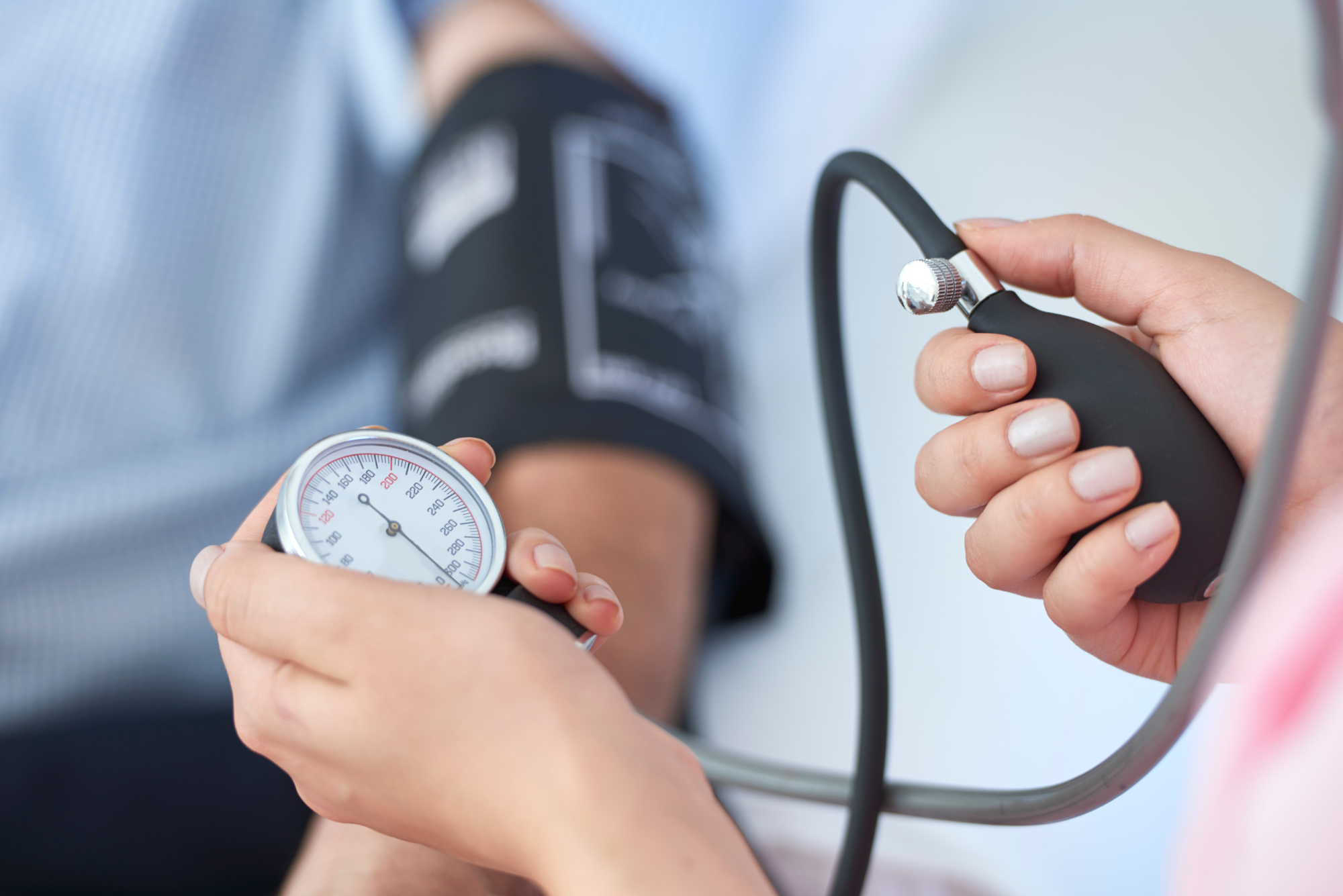 Healthcare professional taking patient’s blood pressure using manual sphygmomanometer and stethoscope in clinical setting.