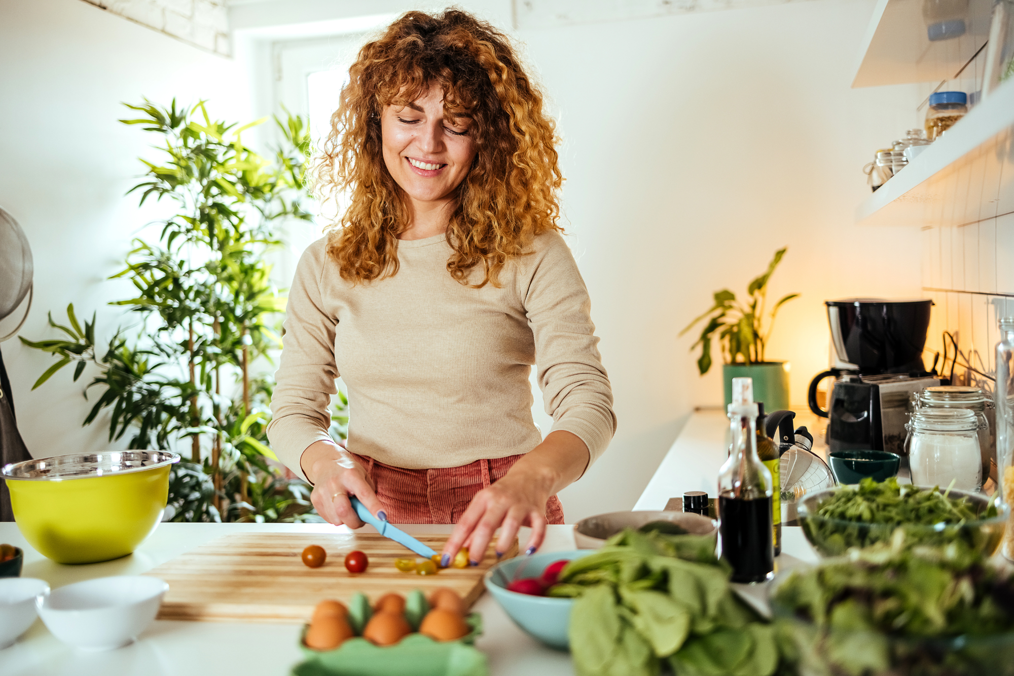 A smiling woman chops fresh vegetables in a bright room.