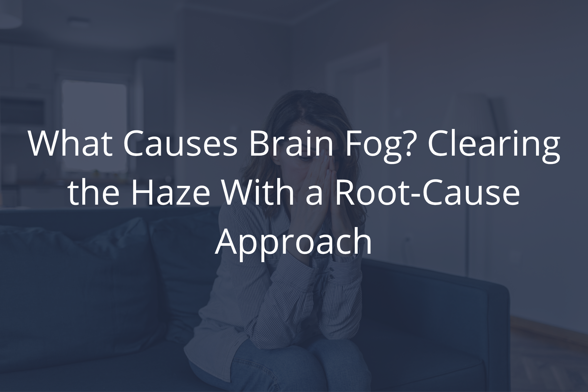 Woman sitting on a couch with her hands pressed to her face, illustrating what causes brain fog.