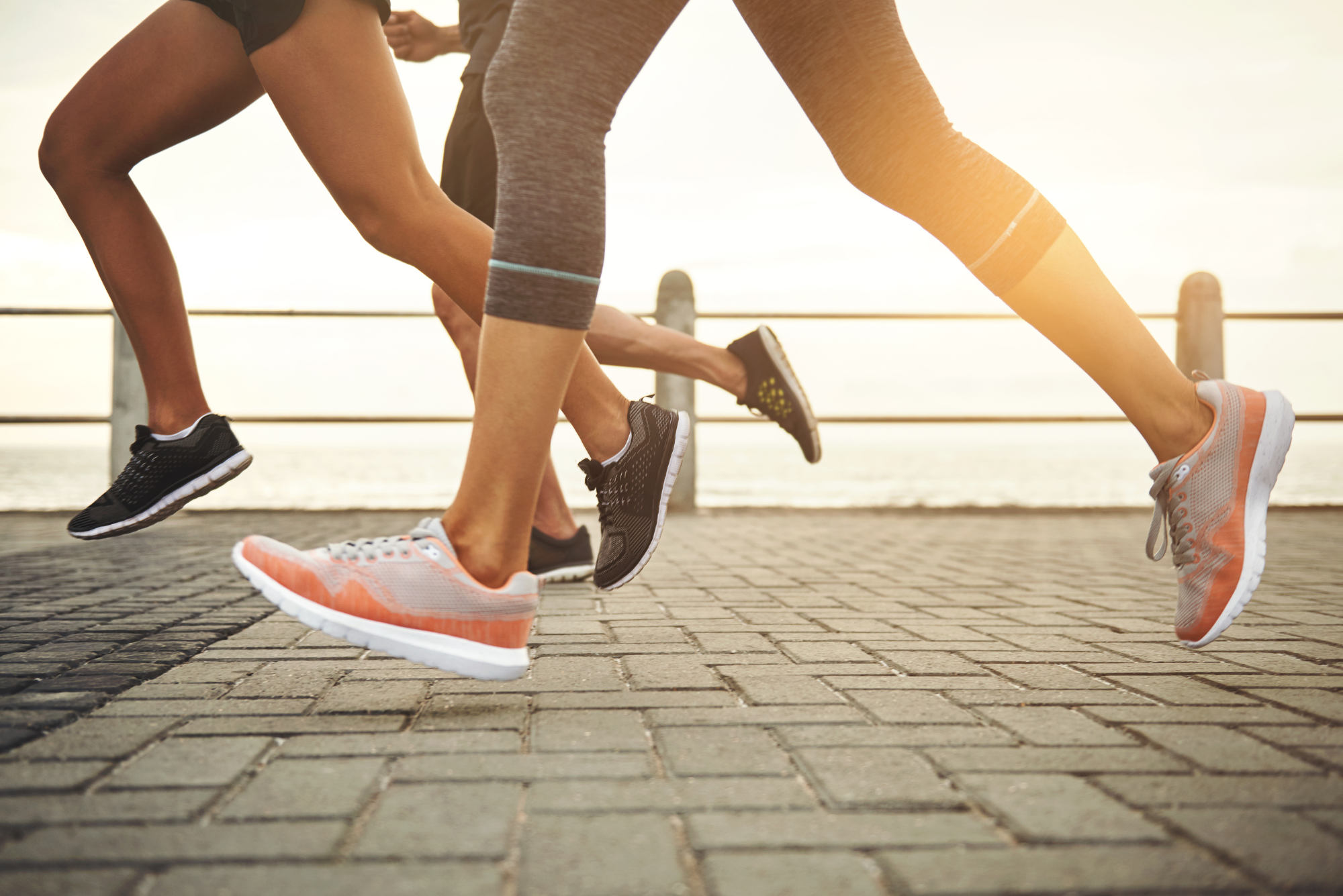 Close-up of three runners' feet and legs in motion on a waterfront path.