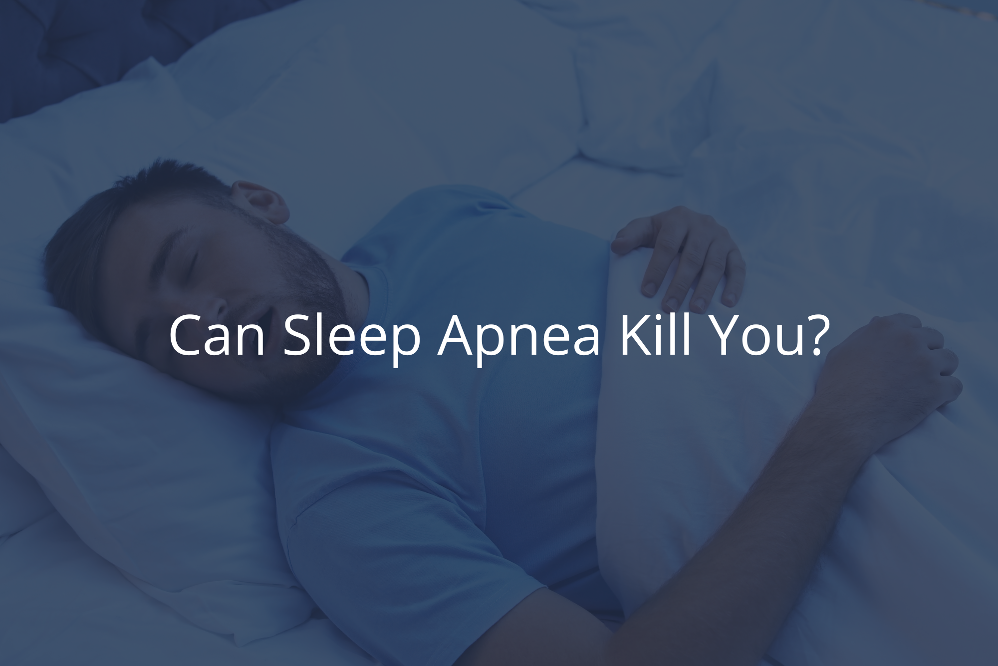 A bearded man in a blue shirt sleeps on his back with his mouth open, snoring, a sign of sleep apnea.